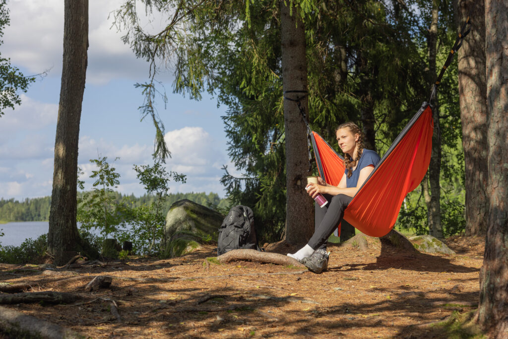 nuori nainen lepäilee riippumatossa järven rannalla